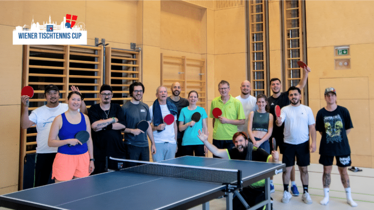 Großes Gruppenfoto aller Teilnehmer:innen des Wiener Tischtennis Cups in der Tischtennis-Halle; Menschen unterschiedlichen Alters stehen gemeinsam mit ihren Schlägern an den Platten.