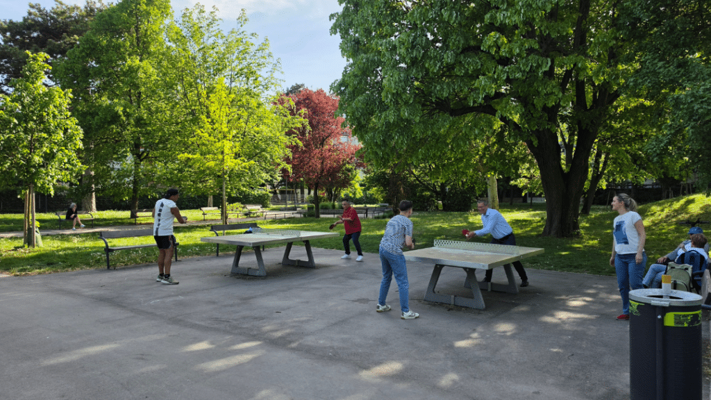 Tischtennis in Wien Floridsdorf mit Tischtennis im Park: Motivierte Hobbyspieler stehen bei strahlendem Sonnenschein an einer öffentlichen Outdoor-Tischtennisplatte im Grätzl und liefern sich beim Saisonauftakt 2026 ein spannendes Match.